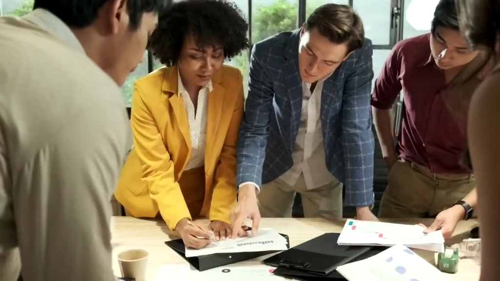 A cross-disciplinary team reviews plans around a standing table.