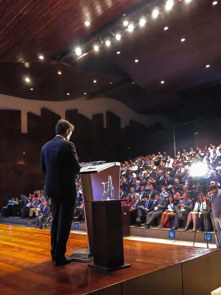A presenter addresses a substantial professional audience from a lectern.