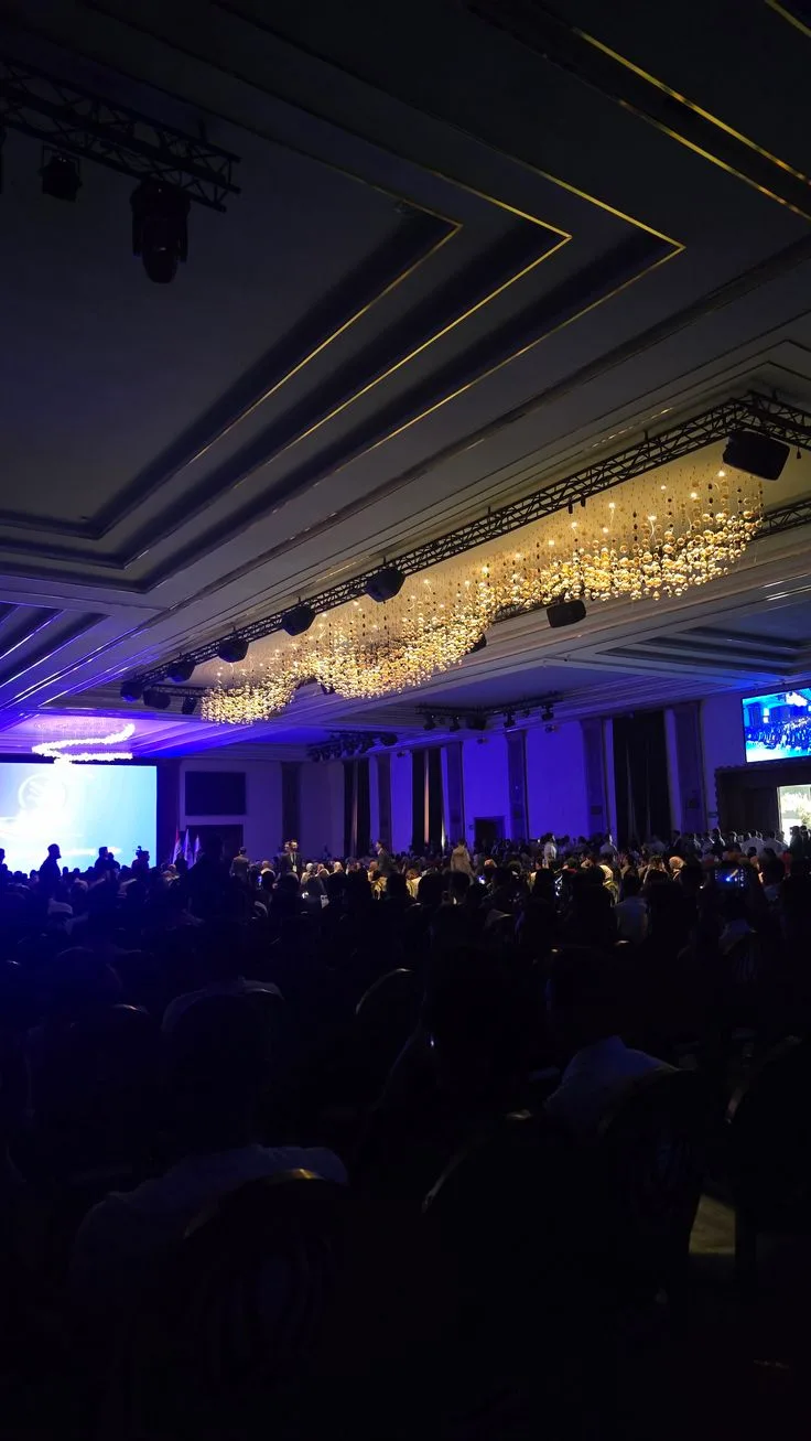 A large audience gathers in a blue-lit conference auditorium.
