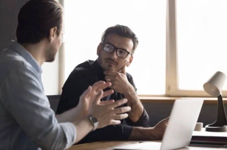 Two professionals discuss work beside a laptop.