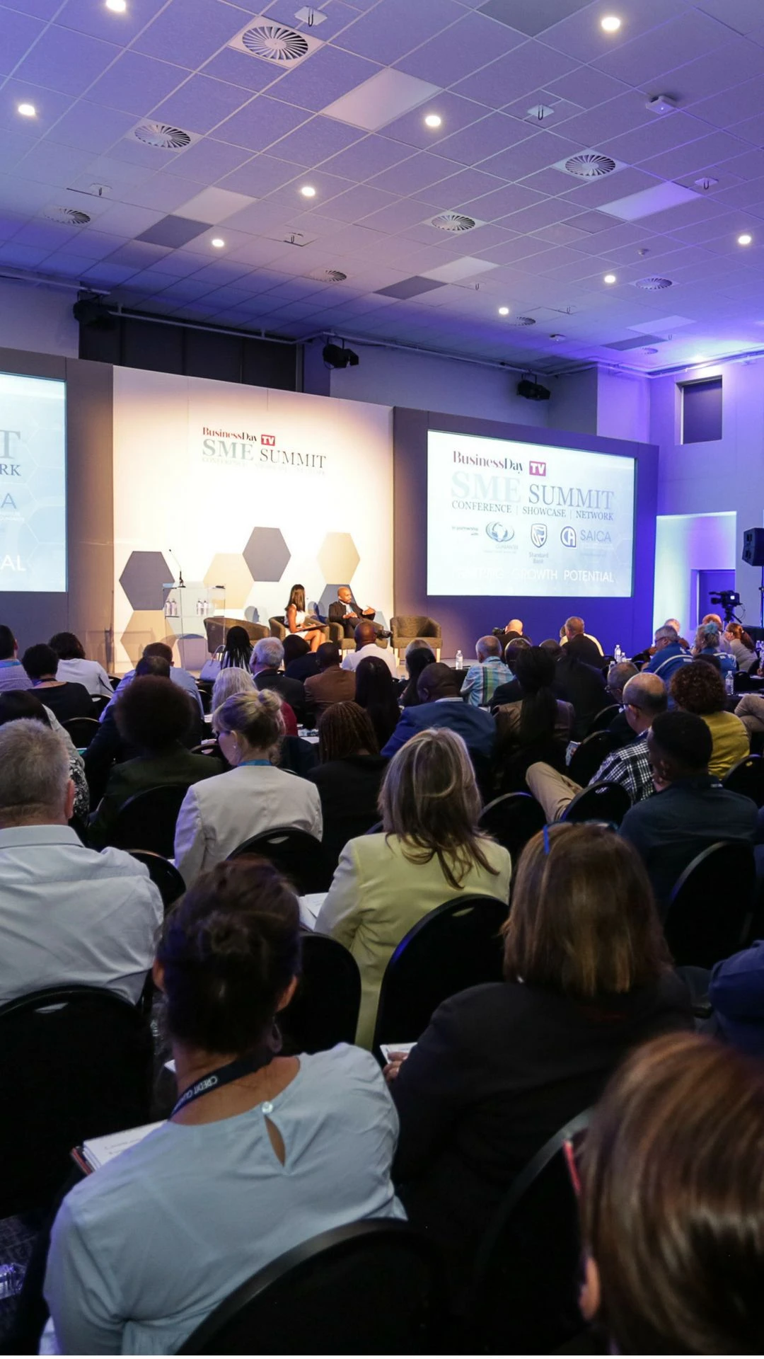 An audience gathers in a professional conference environment.